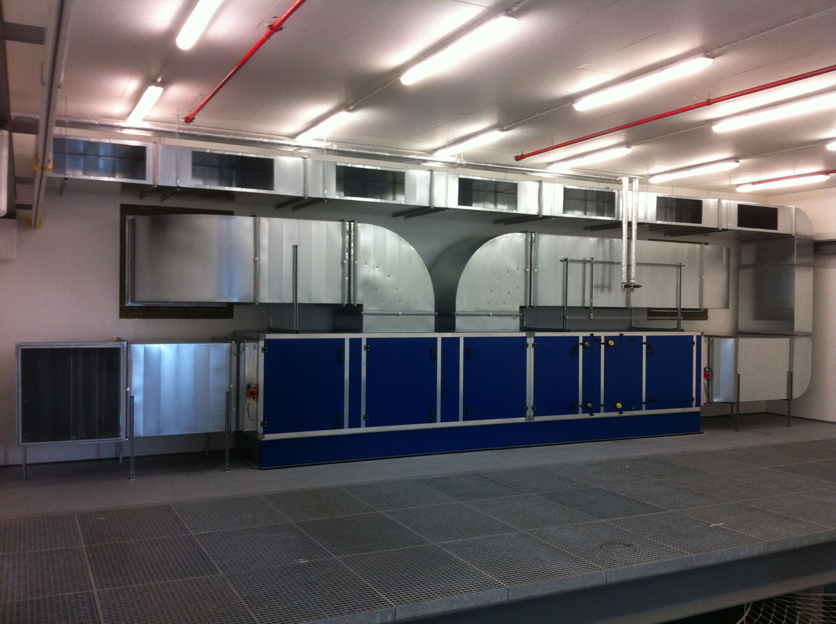 Industrielle Lüftungsanlage mit blauen Modulen und Luftkanälen in einem hell beleuchteten Technikraum mit weißen Wänden.